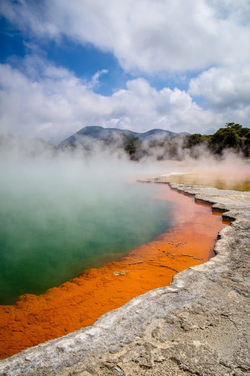 a hot springs pool of water with colorful minerals and steam rising